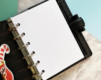 May include: A black leather bound notebook with a white page open. The page is dotted and has a silver ring binder.