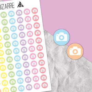 May include: A sheet of colourful camera stickers. The stickers are in a rainbow of colours, including yellow, orange, red, pink, purple, blue, and green. Each sticker features a white camera icon in the centre.