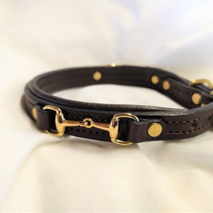 May include: A brown leather dog collar with a gold-toned snaffle bit buckle and decorative studs.
