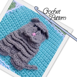 May include: A crochet pattern for a gray dog with a pink nose. The dog is sitting on a blue crochet blanket. The pattern includes a crochet hook.