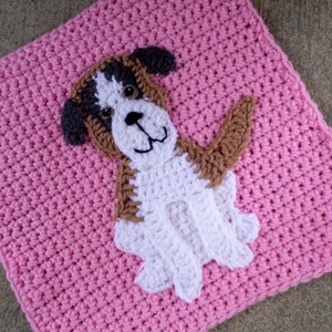 Peut inclure: Un carr&eacute; en crochet rose avec une applique de chien en crochet blanc et marron. Le chien a un nez marron et des yeux noirs.