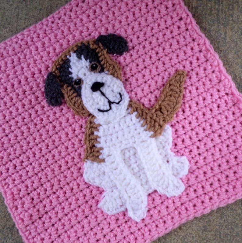 Peut inclure: Un carr&eacute; en crochet rose avec une applique de chien en crochet blanc et marron. Le chien a un nez marron et des yeux noirs.