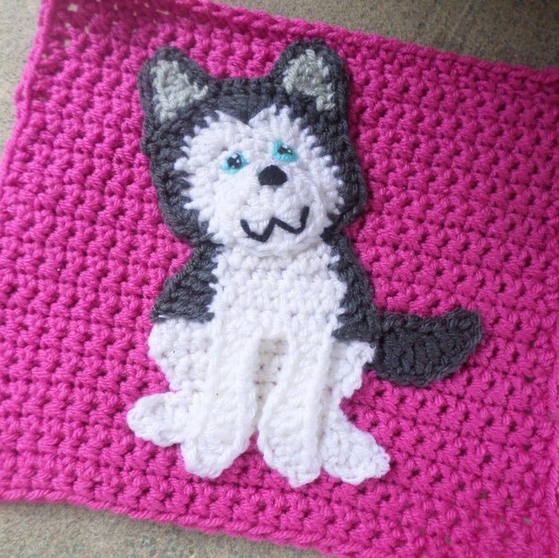 May include: A crocheted husky dog applique in white, gray, and blue on a pink crocheted background.