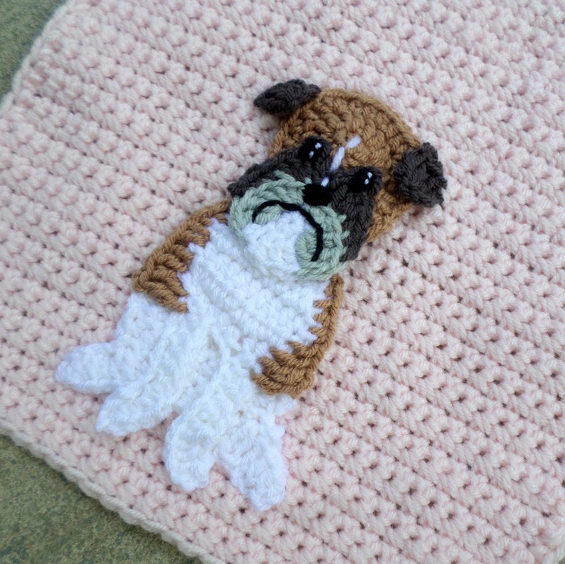 Op de afbeelding: Een roze gebreid deken met een bruine, witte en groene gebreide boxerhond applique.