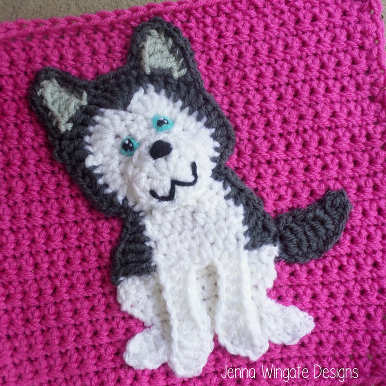 May include: A white and gray crocheted husky dog applique with blue eyes on a pink crocheted background. The applique is a great addition to a baby blanket or other crocheted project.