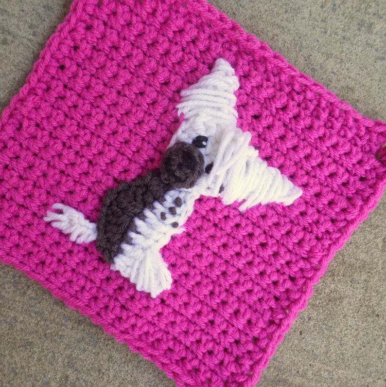 May include: A pink crocheted square with a white and brown crocheted dog applique.