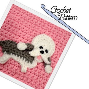 May include: A crocheted pink blanket with a white and gray crocheted dog applique. The dog has black eyes and a pink tongue.