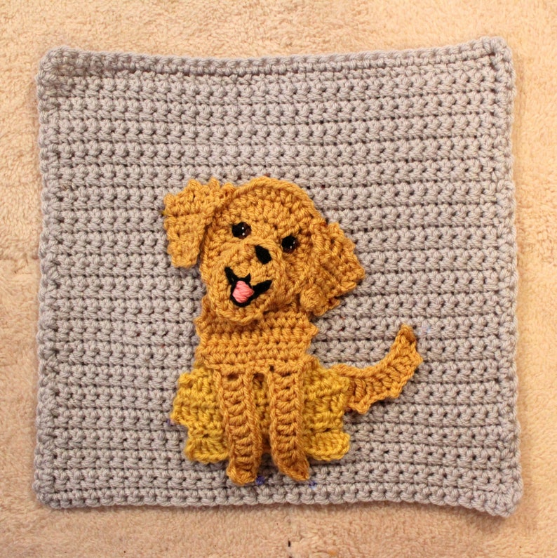 Peut inclure: Un carr&eacute; en crochet gris avec une applique de chien en crochet jaune au centre. Le chien sourit avec une langue rose.