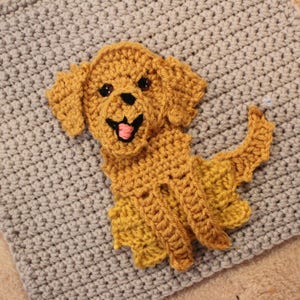 Peut inclure: Une applique en crochet repr&eacute;sentant un chiot golden retriever avec un corps brun clair et un fond gris clair.