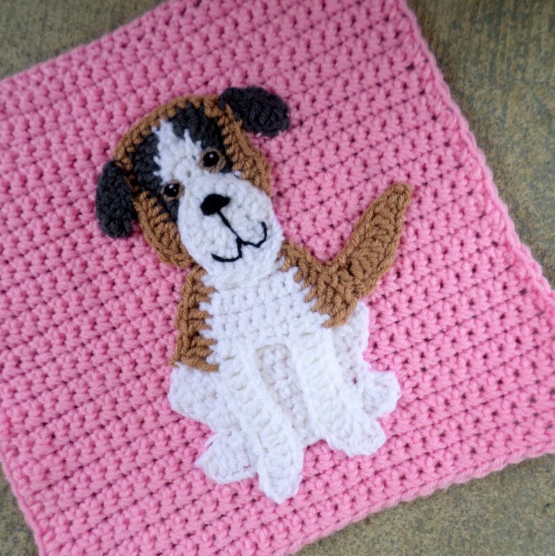 Peut inclure: Un carr&eacute; crochet&eacute; avec une applique de chien marron, blanc et gris. Le chien est assis, les pattes avant lev&eacute;es et la queue enroul&eacute;e sur le c&ocirc;t&eacute;. Le carr&eacute; est rose.