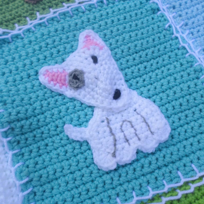Pode incluir: Uma aplica&ccedil;&atilde;o de c&atilde;o de croch&ecirc; branco com orelhas cor-de-rosa e detalhes cinzentos e pretos, sobre um fundo de croch&ecirc; turquesa.