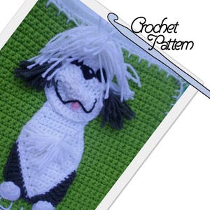 May include: A crocheted white and black dog with a pink tongue, sitting on a green crocheted background. The image includes the text "Crochet Pattern".