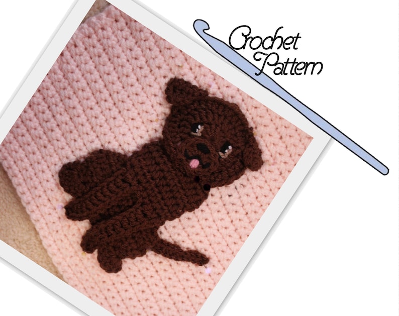 May include: A crochet pattern for a brown dog applique. The dog is sitting on a pink crocheted background. The pattern includes a crochet hook.