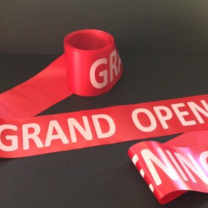 May include: Red ribbon with the words "GRAND OPENING" printed in white.
