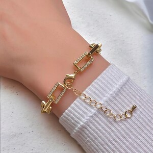 May include: Gold chain bracelet with a square link design. The links are accented with small clear rhinestones.