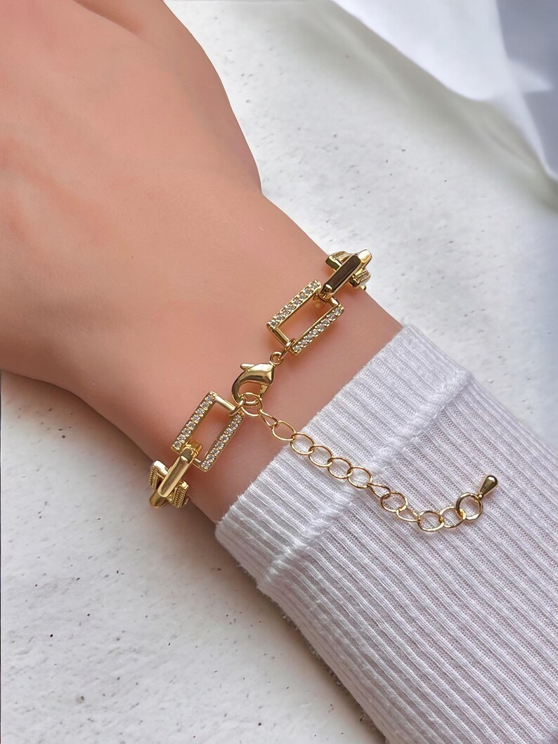 May include: Gold chain bracelet with a square link design. The links are accented with small clear rhinestones.