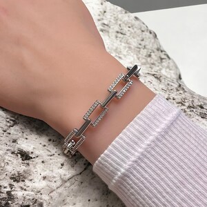 May include: A silver bracelet with a chain link design. Each link is adorned with small, clear rhinestones.