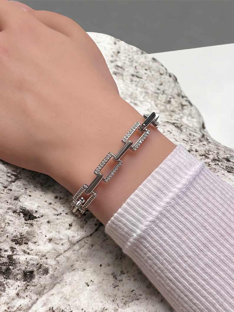 May include: A silver bracelet with a chain link design. Each link is adorned with small, clear rhinestones.