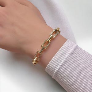 May include: Gold chain bracelet with square links, each link is encrusted with small clear rhinestones.
