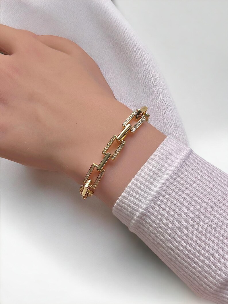 May include: Gold chain bracelet with square links, each link is encrusted with small clear rhinestones.