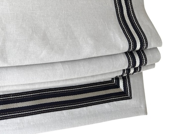 May include: White roman shade with black and white striped trim. The trim has a beaded detail.