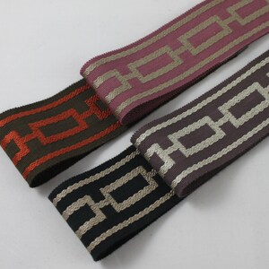 May include: Three different patterned ribbon trims with a geometric design. The ribbons are in shades of brown, pink, and black with gold accents.