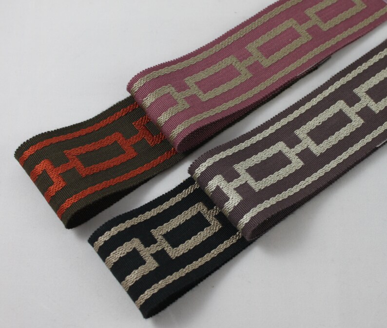 May include: Three different patterned ribbon trims with a geometric design. The ribbons are in shades of brown, pink, and black with gold accents.