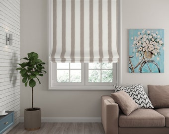 May include: A beige and white striped roman shade is partially raised, revealing a window with two panes. The shade is in a living room setting with a brown sofa, a potted plant, and a painting on the wall.