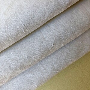 May include: A stack of three white linen fabric panels. The fabric is smooth and has a subtle texture. The panels are folded in thirds and the edges are visible. The fabric is a light cream color.