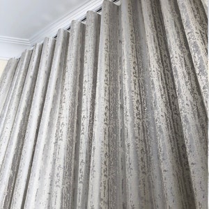 Textured silver-gray drapery in deep ripple fold waves on a white ceiling-mounted s-fold track - custom wave fold curtains with crown molding above