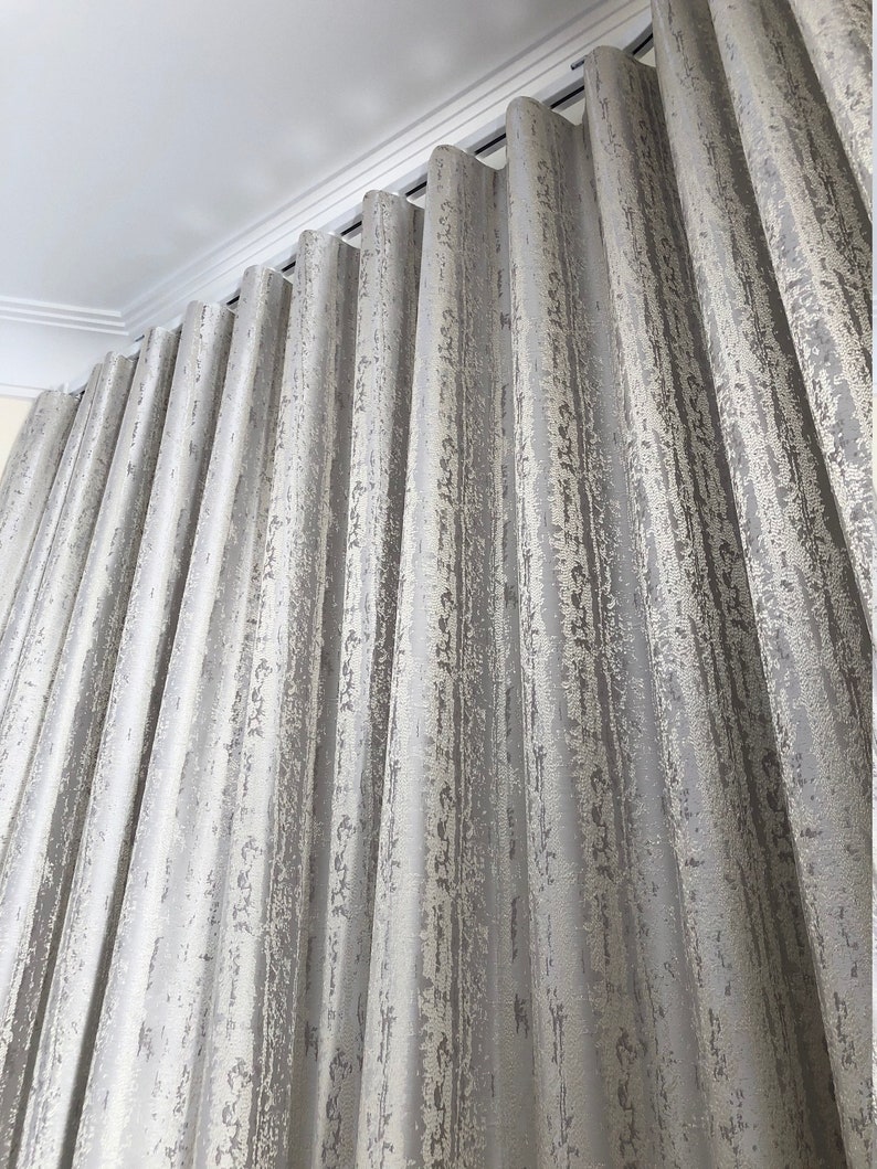 Textured silver-gray drapery in deep ripple fold waves on a white ceiling-mounted s-fold track - custom wave fold curtains with crown molding above
