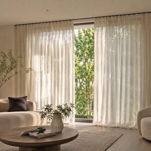 Floor-to-ceiling cream sheer curtains in soft ripple fold waves on a ceiling mounted aluminum drapery track in a bright modern living room with garden view