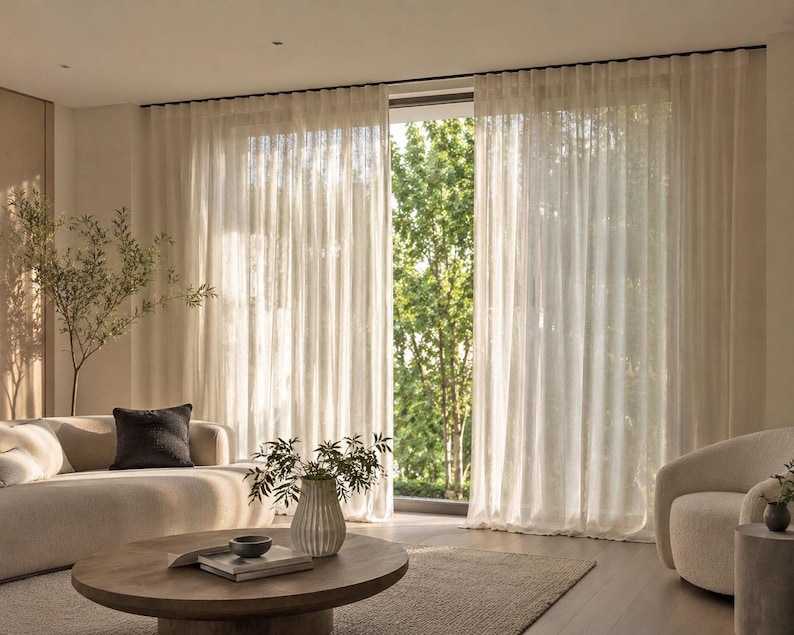 Floor-to-ceiling cream sheer curtains in soft ripple fold waves on a ceiling mounted aluminum drapery track in a bright modern living room with garden view