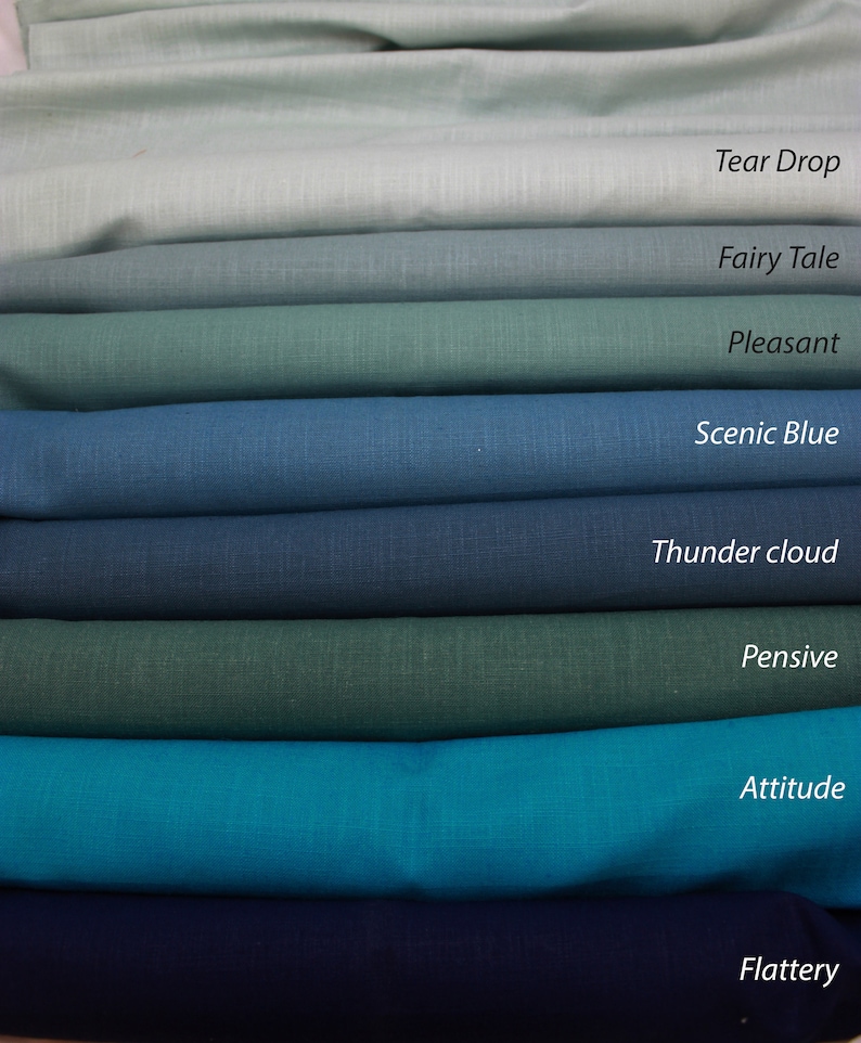 May include: A stack of eight fabric swatches in various shades of blue and green, with names for each color written below them: Tear Drop, Fairy Tale, Pleasant, Scenic Blue, Thunder Cloud, Pensive, Attitude, and Flattery.