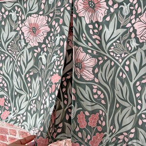 May include: A green fabric with a pink floral pattern. The fabric has a white trim and is folded in half.