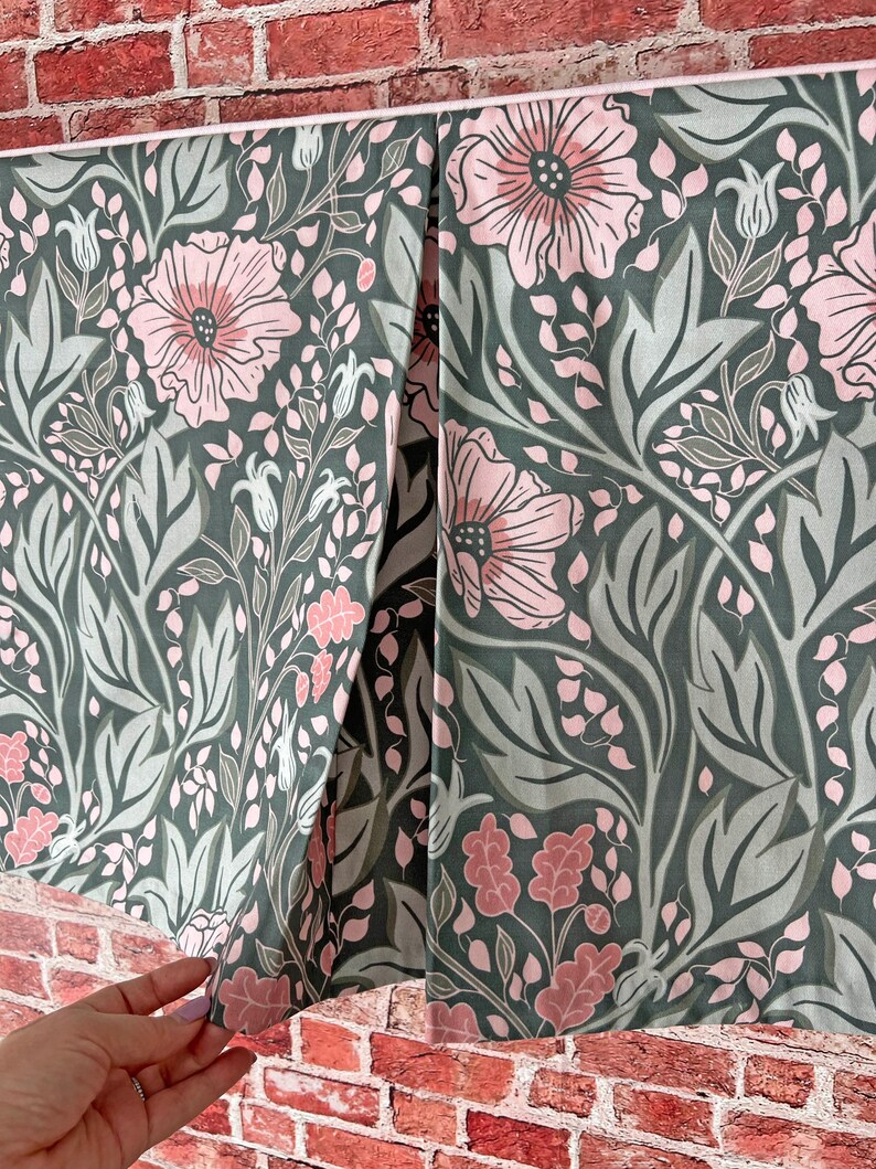 May include: A green fabric with a pink floral pattern. The fabric has a white trim and is folded in half.