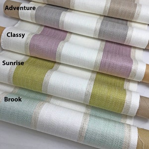 K&ouml;nnte beinhalten: F&uuml;nf Rollen Stoff mit verschiedenen farbigen Streifen. Der Stoff ist wei&szlig; mit einem Fischgr&auml;tenmuster und einem farbigen Streifen in der Mitte. Die Farben sind beige, grau, rosa, gelb und gr&uuml;n.