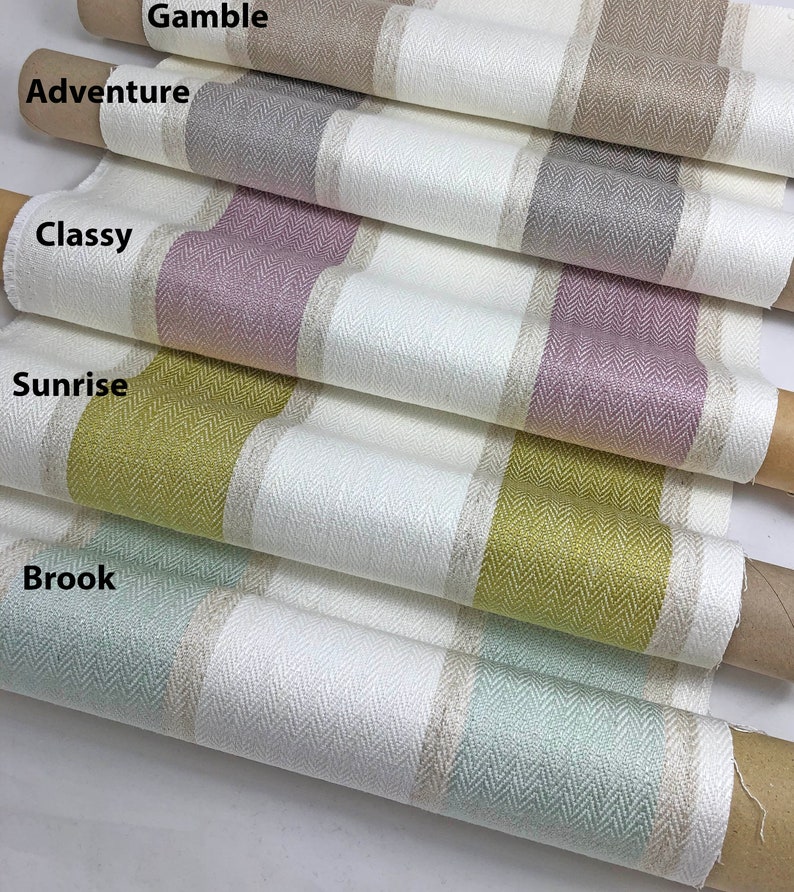 K&ouml;nnte beinhalten: F&uuml;nf Rollen Stoff mit verschiedenen farbigen Streifen. Der Stoff ist wei&szlig; mit einem Fischgr&auml;tenmuster und einem farbigen Streifen in der Mitte. Die Farben sind beige, grau, rosa, gelb und gr&uuml;n.
