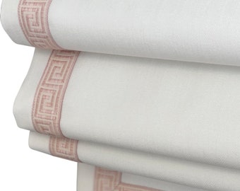 May include: White roman shade with a pink greek key border.