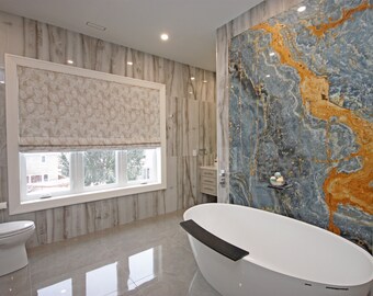 May include: A white bathtub with a black ledge sits in a bathroom with gray tiled walls and a large blue and gold marble wall behind it.