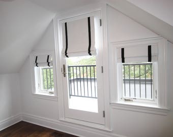 May include: White roman shades with black trim on three windows, including a door leading to a balcony with a black railing.