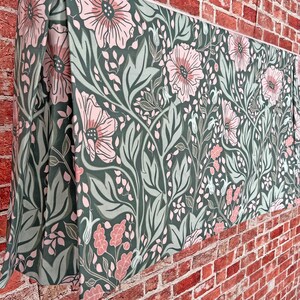 May include: A green and pink floral patterned fabric valance with a pleated edge. The valance is hanging on a brick wall.