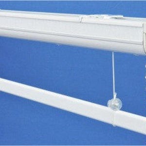 May include: White window blind with a chain mechanism. The blind is mounted to the ceiling and has a white metal track.
