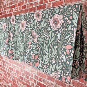 May include: A green and pink floral valance with a repeating pattern of flowers and leaves. The valance is made of fabric and has a pleated design.