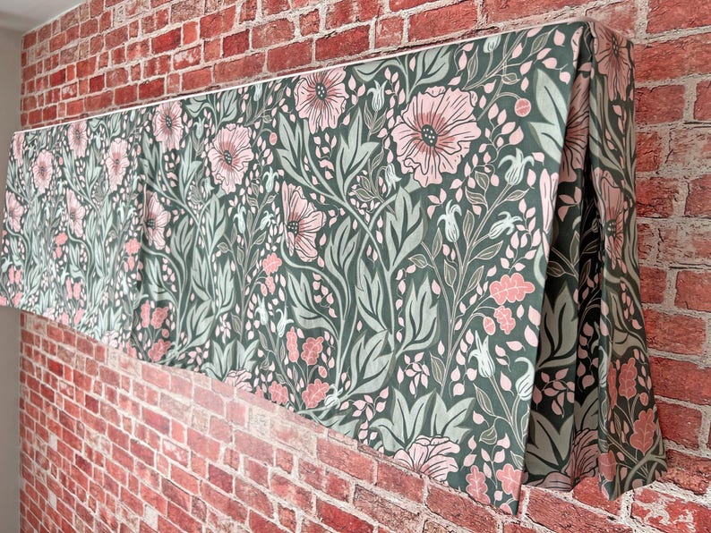 May include: A green and pink floral valance with a repeating pattern of flowers and leaves. The valance is made of fabric and has a pleated design.