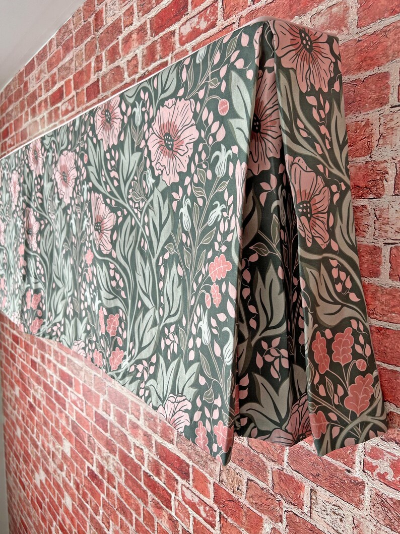 May include: A green and pink floral valance with a repeating pattern of flowers and leaves. The valance is made of fabric and has a pleated design.