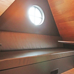 May include: A brown leather bench with a dark brown wood table in a room with a wood ceiling and a round window.