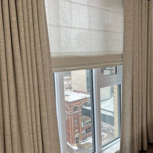 Camel drapery panels on a ceiling mount ripple fold track layered over a natural linen roman shade - custom wave fold curtain hardware in a city apartment window