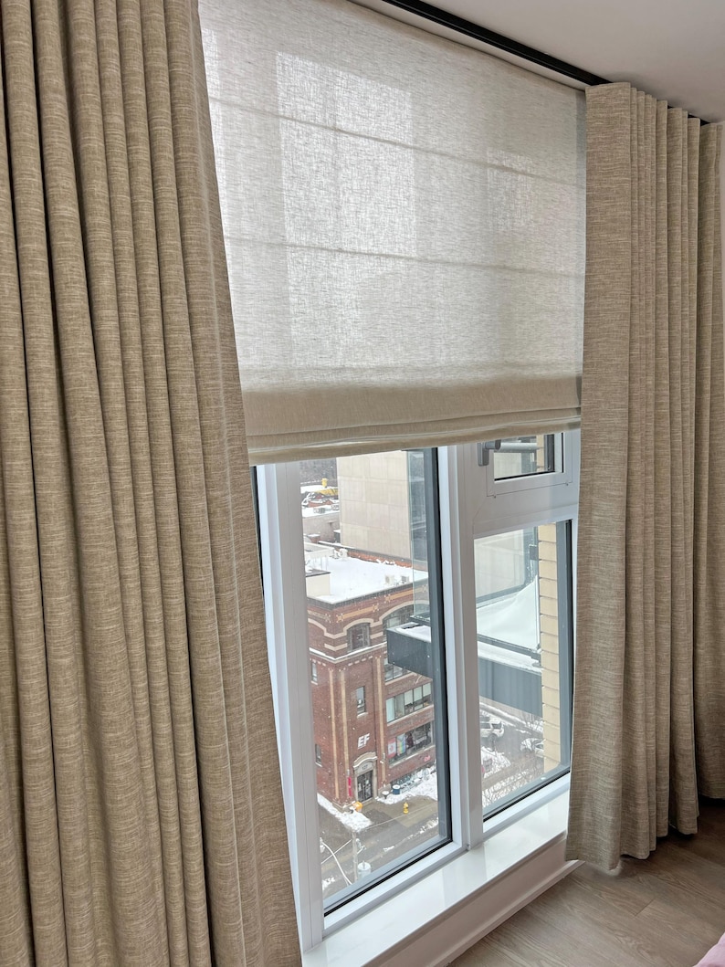 Camel drapery panels on a ceiling mount ripple fold track layered over a natural linen roman shade - custom wave fold curtain hardware in a city apartment window