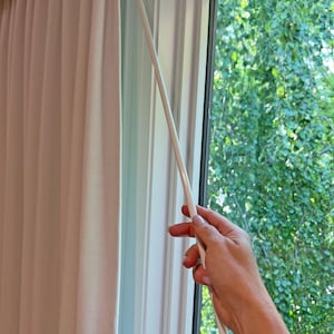 May include: A white curtain pole with a white cord attached to it. The cord is being pulled by a hand to open the curtain.